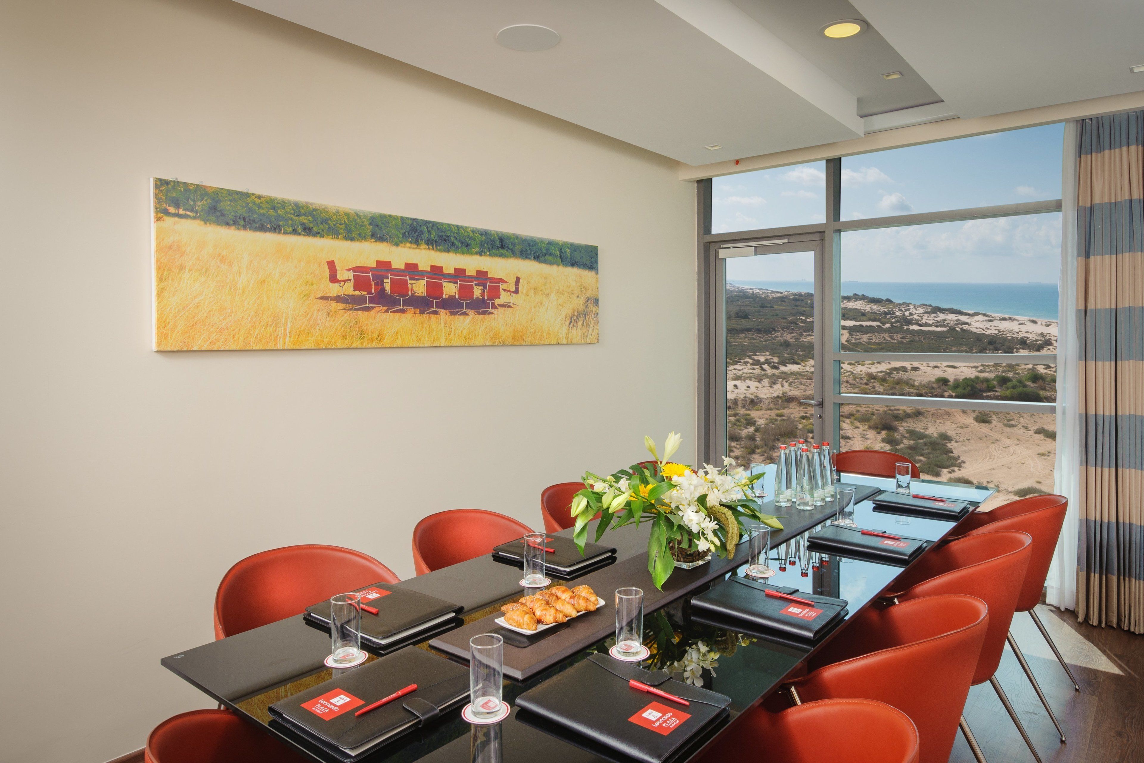 A conference room with a long table, red chairs, and a large window offering a view of the desert landscape.