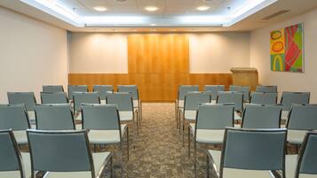 A conference room with rows of chairs facing a podium, carpeted floor, and a ceiling with recessed lighting.
