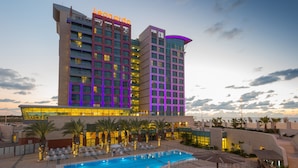 A hotel with a swimming pool, palm trees, and a view of the ocean. - Leonardo Plaza Ashdod (Ashdod)