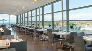A modern restaurant with large windows, wooden flooring, and a view of the city. - Leonardo Plaza Ashdod (Ashdod)