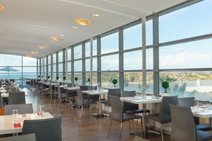 A modern restaurant with large windows, wooden flooring, and a view of the city.