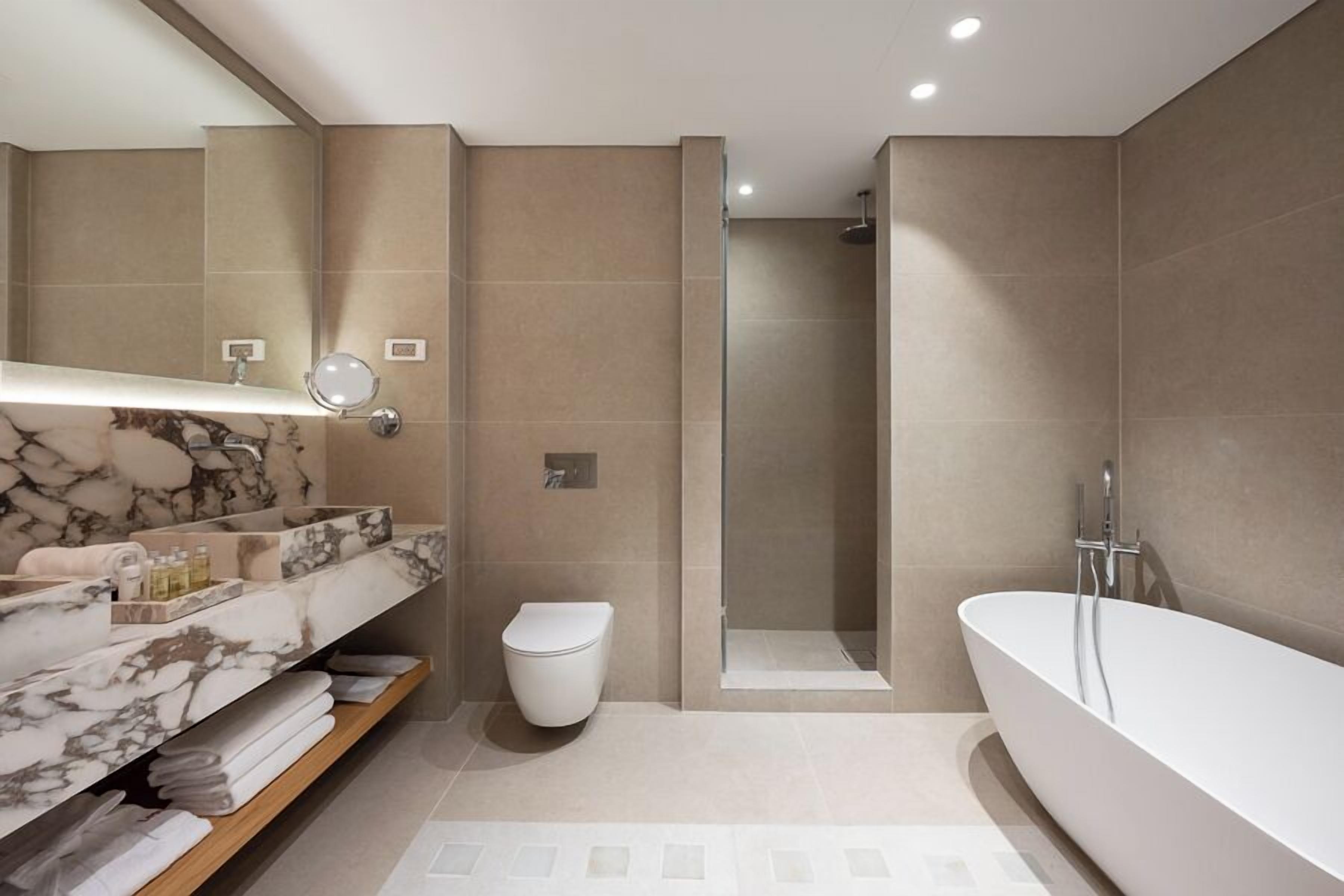 A modern bathroom with a marble vanity, a toilet, a walk-in shower, and a freestanding bathtub.