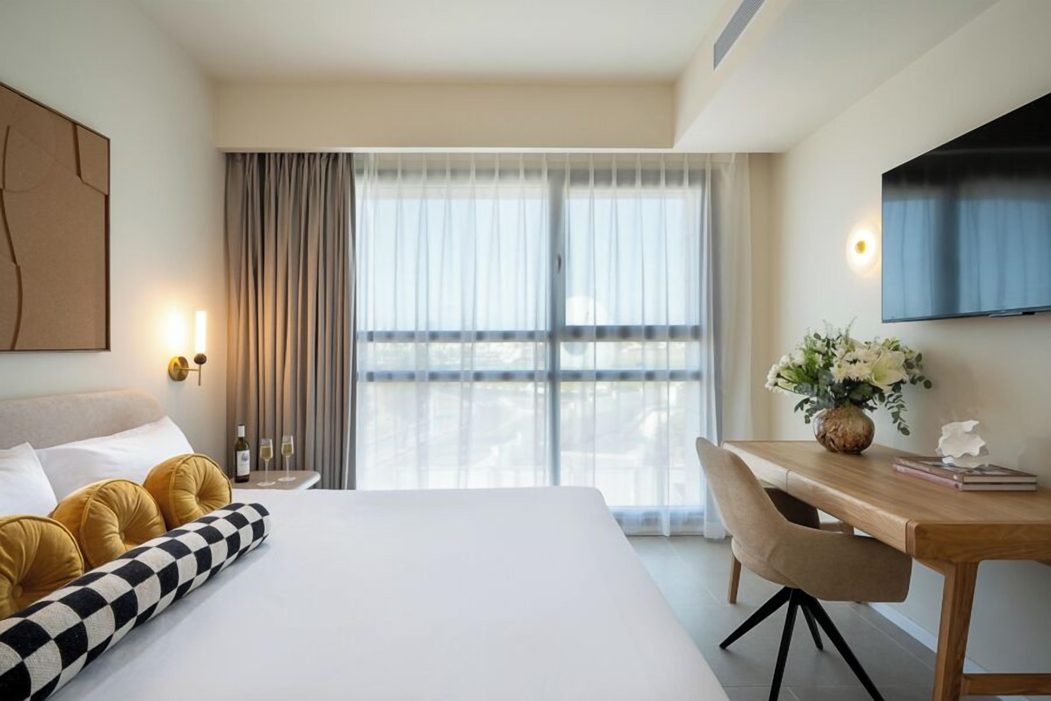 Une chambre d’hôtel avec un lit, un bureau, une chaise, une télévision et une fenêtre avec des rideaux.