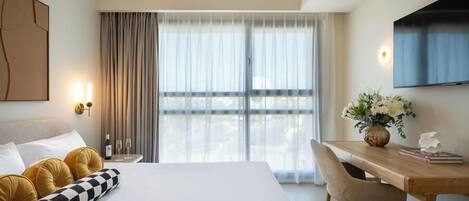 Une chambre d’hôtel avec un lit, un bureau, une chaise, une télévision et une fenêtre avec des rideaux.
