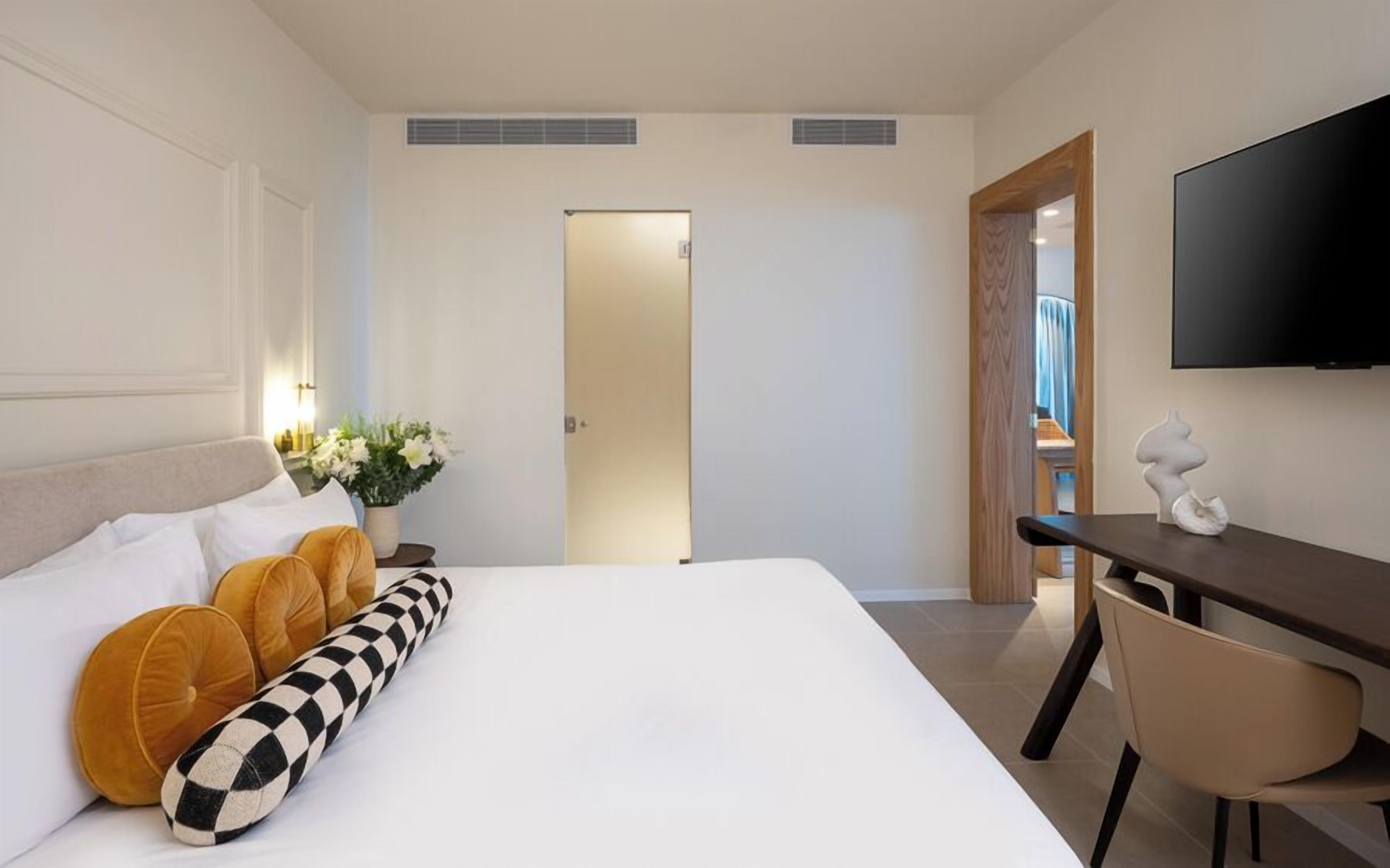 Et hotelværelse med en seng, et skrivebord, en stol, et fjernsyn og en dør til et badeværelse.