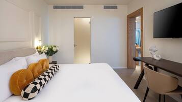 A hotel room with a bed, a desk, a chair, a TV, and a door leading to a bathroom.