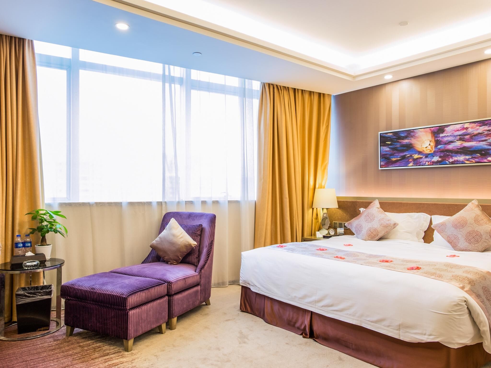 A hotel room with a large bed, a chair, a small table, and a window with curtains.
