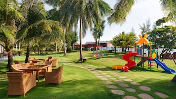 A playground with slides and swings, surrounded by palm trees and outdoor furniture.