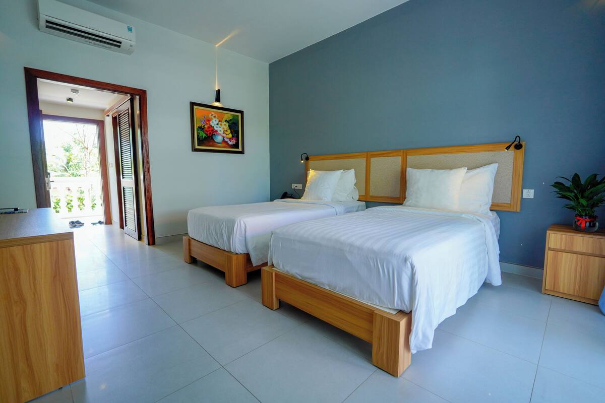 A bedroom with two single beds, a wooden desk, a small bedside table, and a potted plant.