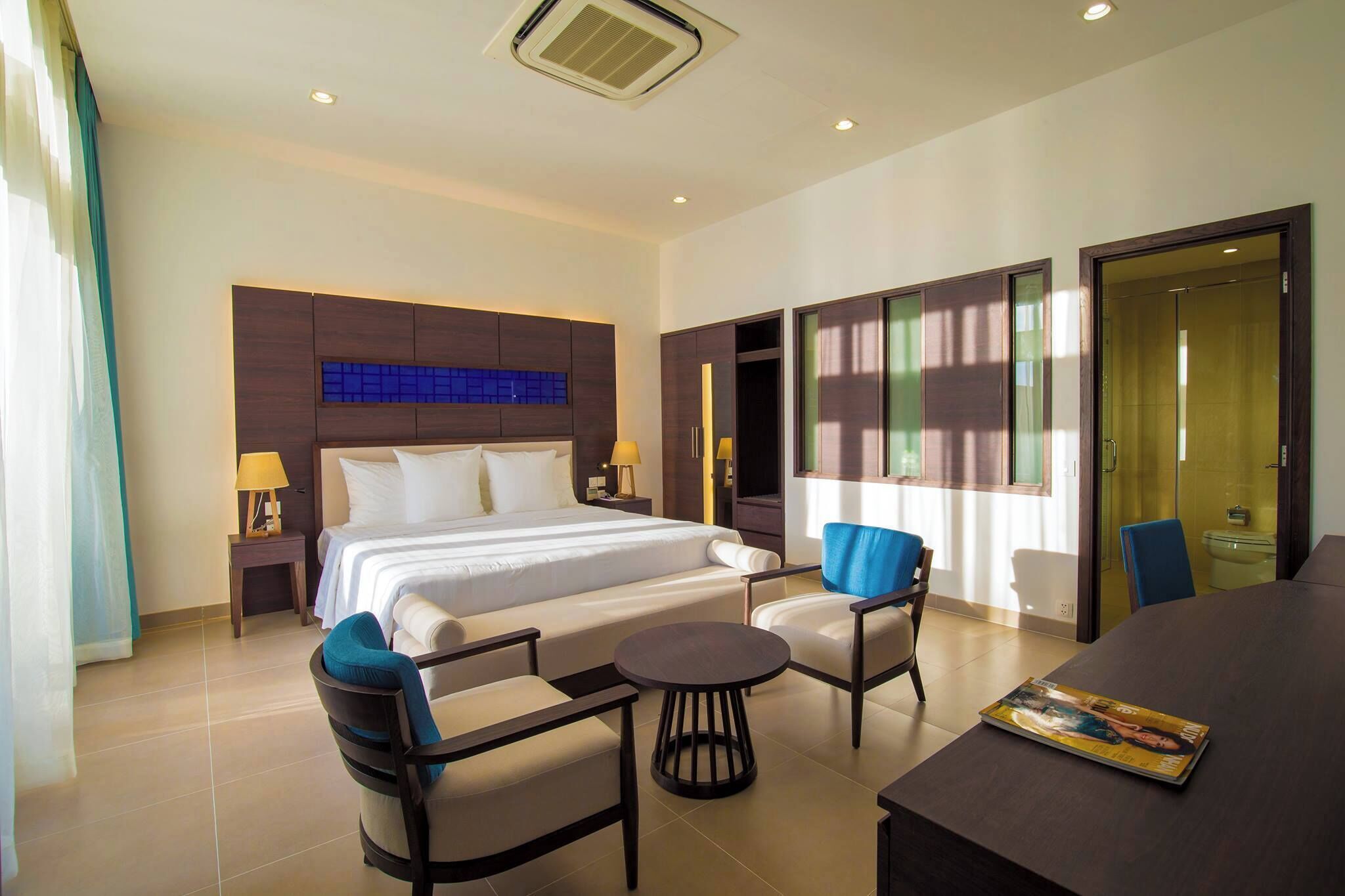 Habitación de hotel con una cama grande, dos sillones, una mesita redonda y una mesa de comedor.