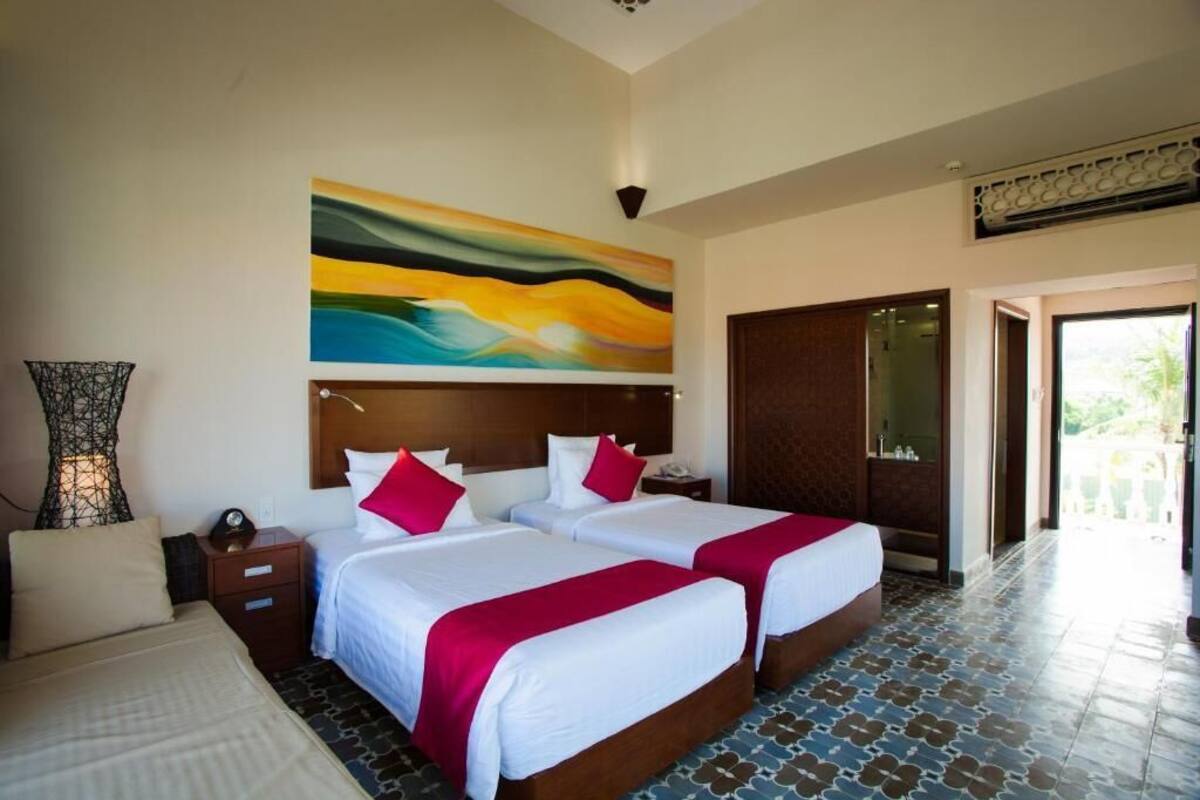 A hotel room with two beds, a large abstract painting on the wall, a nightstand, and a view of the outside.