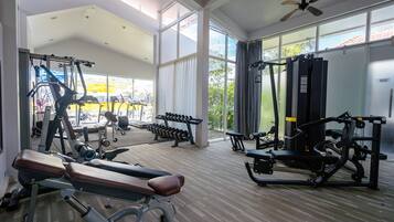 A spacious gym with various exercise equipment, large windows, and a ceiling fan.