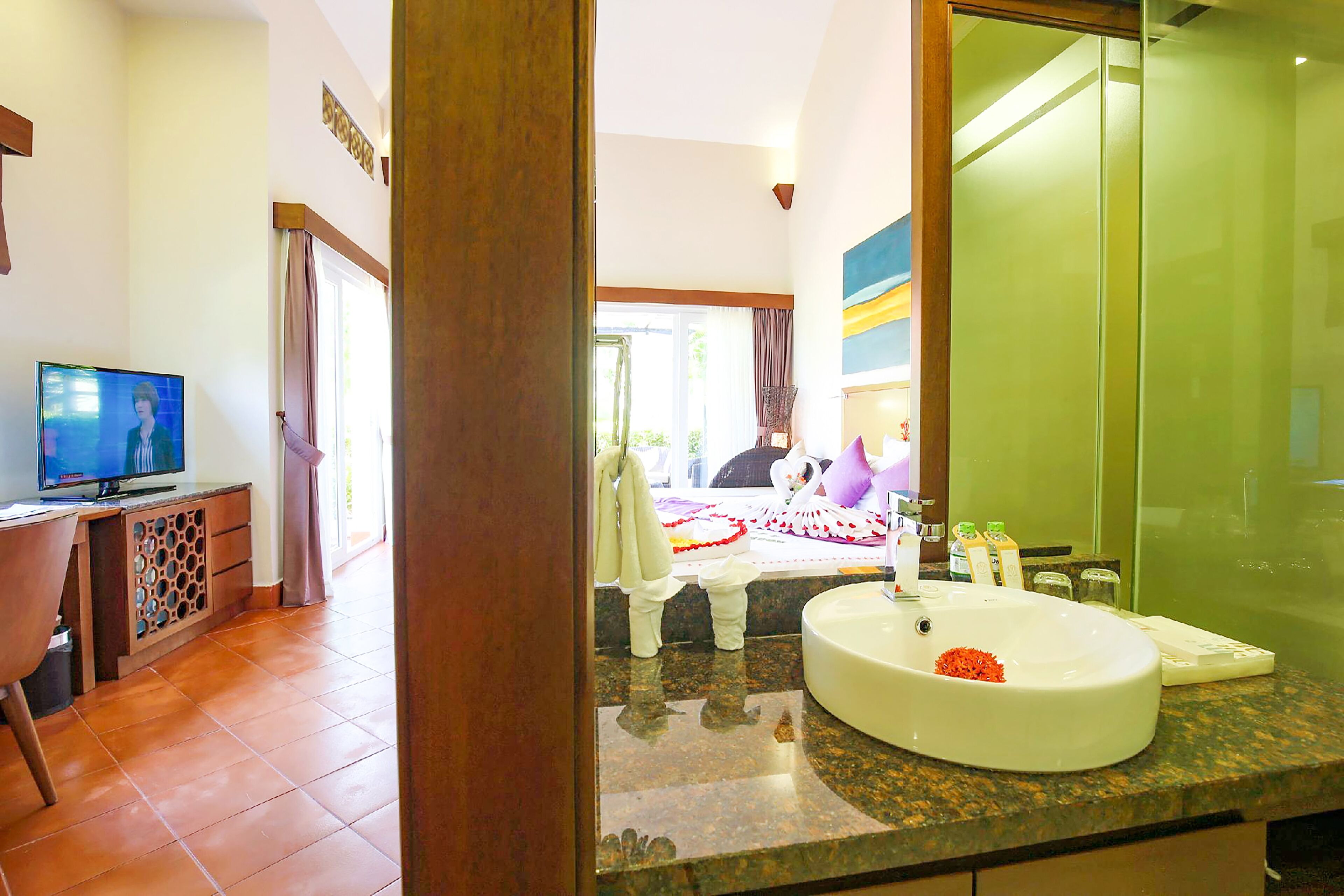 Un bagno d'albergo con uno specchio grande, un lavandino e una televisione nella stanza comunicante.