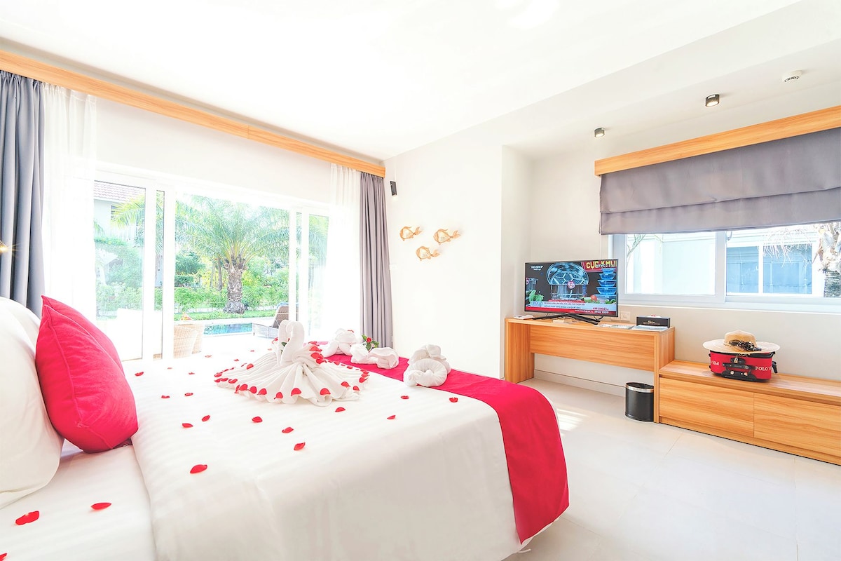 Une chambre d’hôtel équipée d’un lit, d’une télévision, d’un bureau et d’une fenêtre donnant sur un paysage verdoyant.