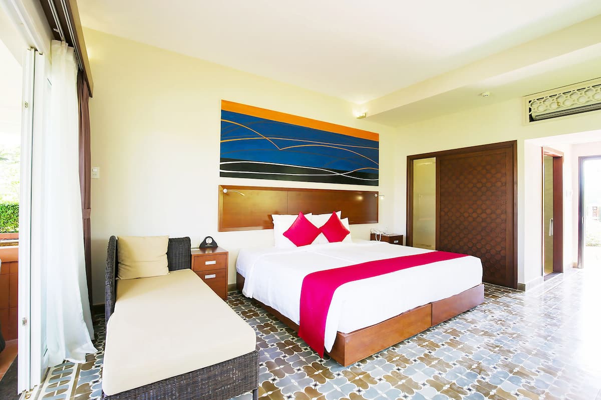 A hotel room with a large bed, a bedside table, a nightstand, a wall-mounted artwork, and a patterned floor.
