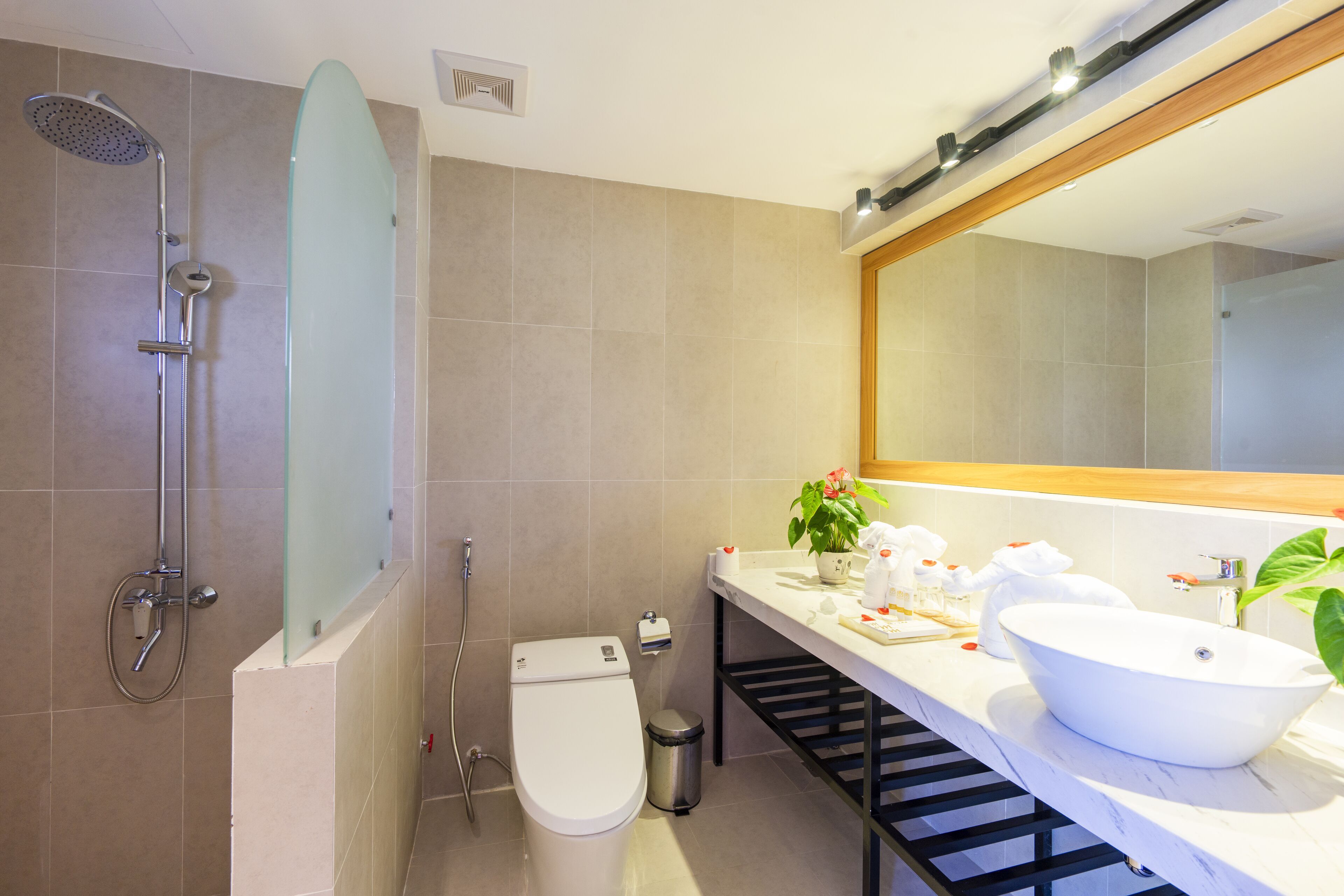 A modern bathroom with a glass shower enclosure, a white toilet, a sink with a large mirror, and a trash bin.