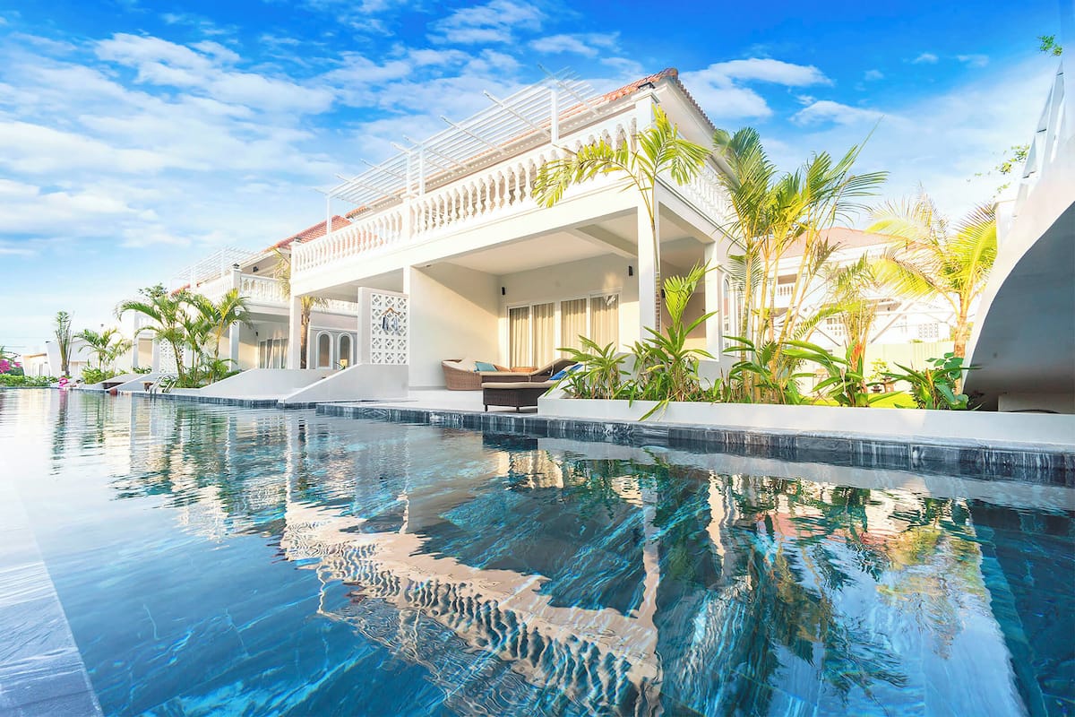 A modern resort with a swimming pool, a covered outdoor area, and tropical plants.