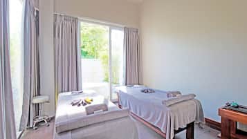 Un cuarto de spa con dos camillas de masaje, un banco de madera y una silla de masajes.