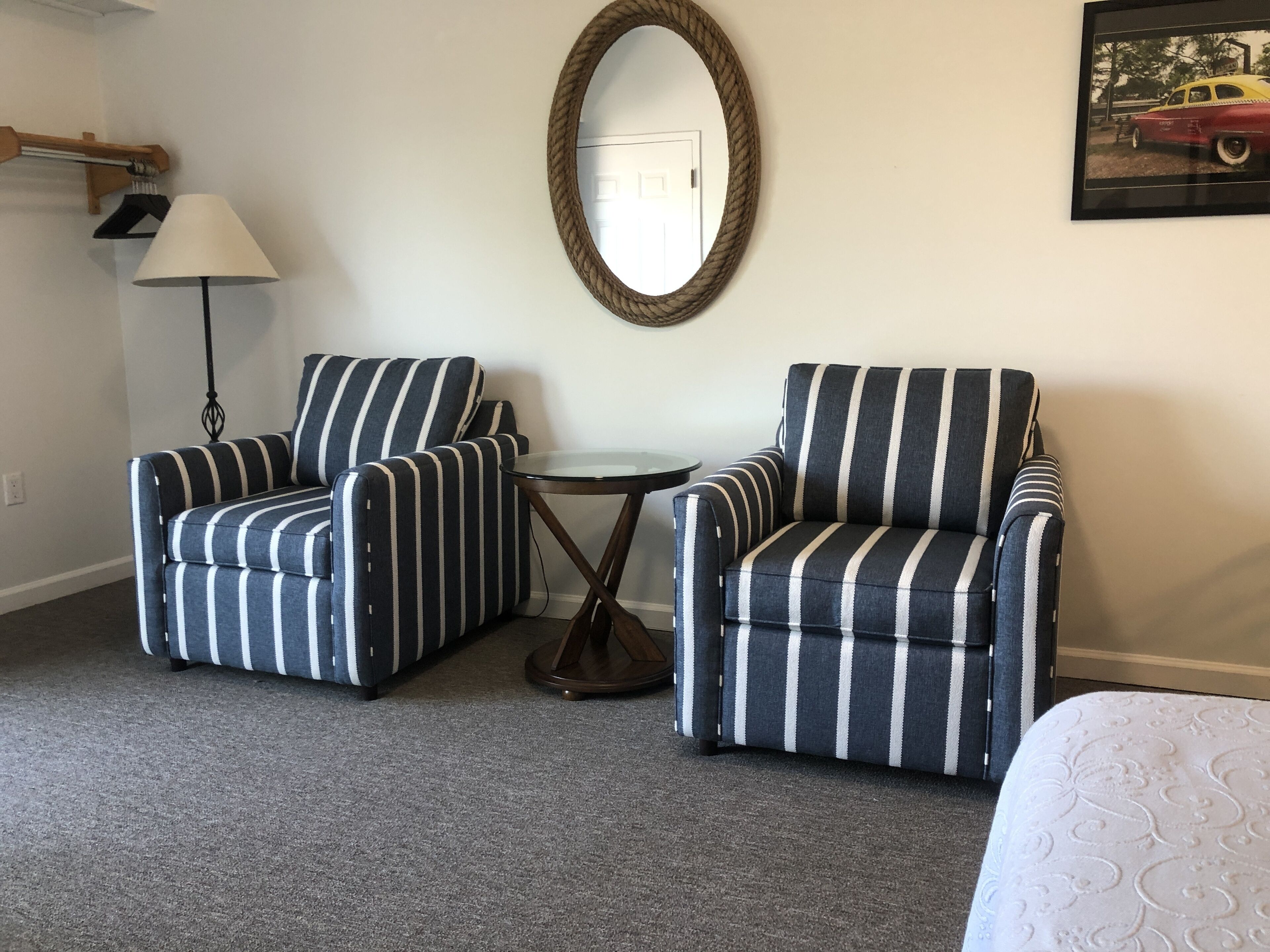 Une pièce comprenant deux fauteuils à rayures, une petite table ronde, une lampe, un miroir et un tableau encadré accroché au mur.