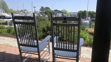 Twee schommelstoelen op een verhard terras, met een jachthaven en boten op de achtergrond.