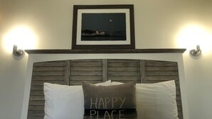 A bed with two pillows, one with "HAPPY PLACE" text, and a framed picture above the bed. - Knapps Narrows Marina & Inn (Sherwood)