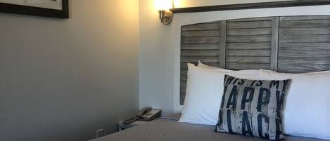 Une chambre d’hôtel avec un grand lit, une tête de lit ornée d’un panneau en bois, une lampe fixée au mur et deux tableaux encadrés.