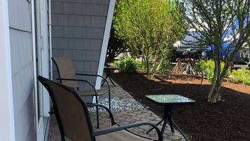An outdoor patio area with hexagonal tiles, a metal chair, a small table, and a garden with various plants and a tree.