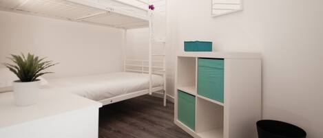 A bunk bed room with a small desk, a potted plant, and a white cabinet with teal drawers.