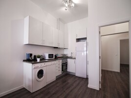 Una cocina compacta con armarios blancos, microondas, lavadora y refrigerador.