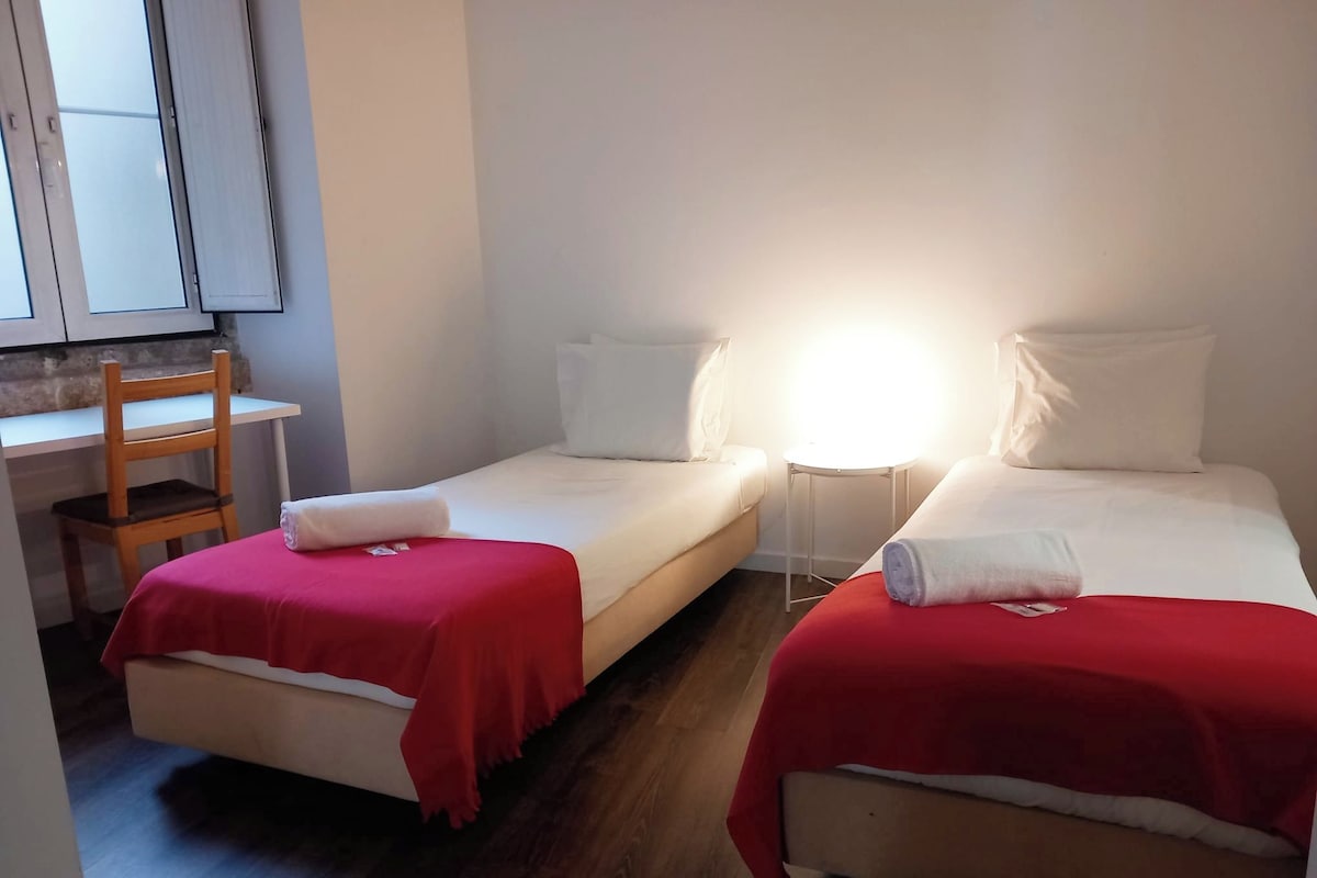 A small, clean room with two single beds, a desk, and a chair.