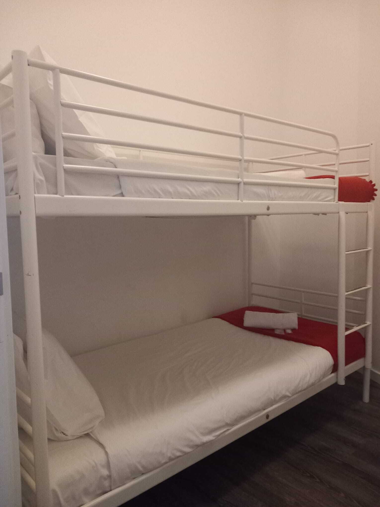 Una cama litera con ropa de cama blanca y una colcha roja.