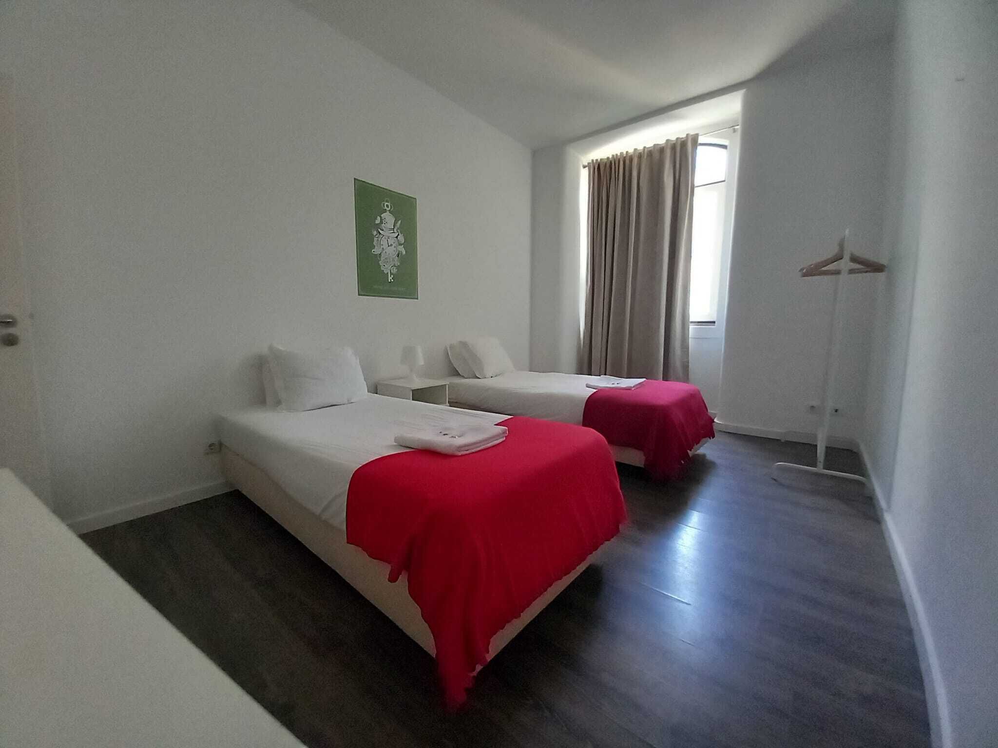 A hotel room with two beds, a green wall decoration, a window with curtains, and a floor lamp.