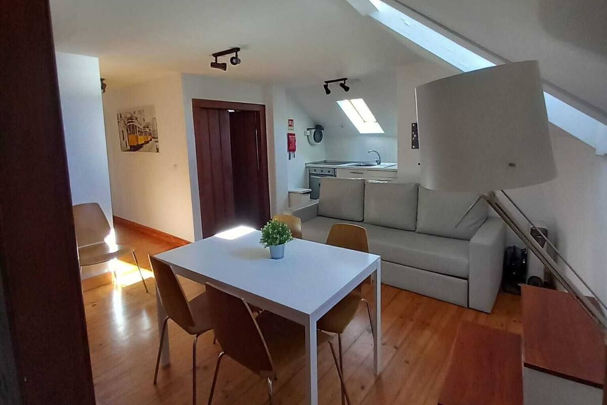 A modern apartment with a dining area, a sofa, a kitchenette, and a skylight.