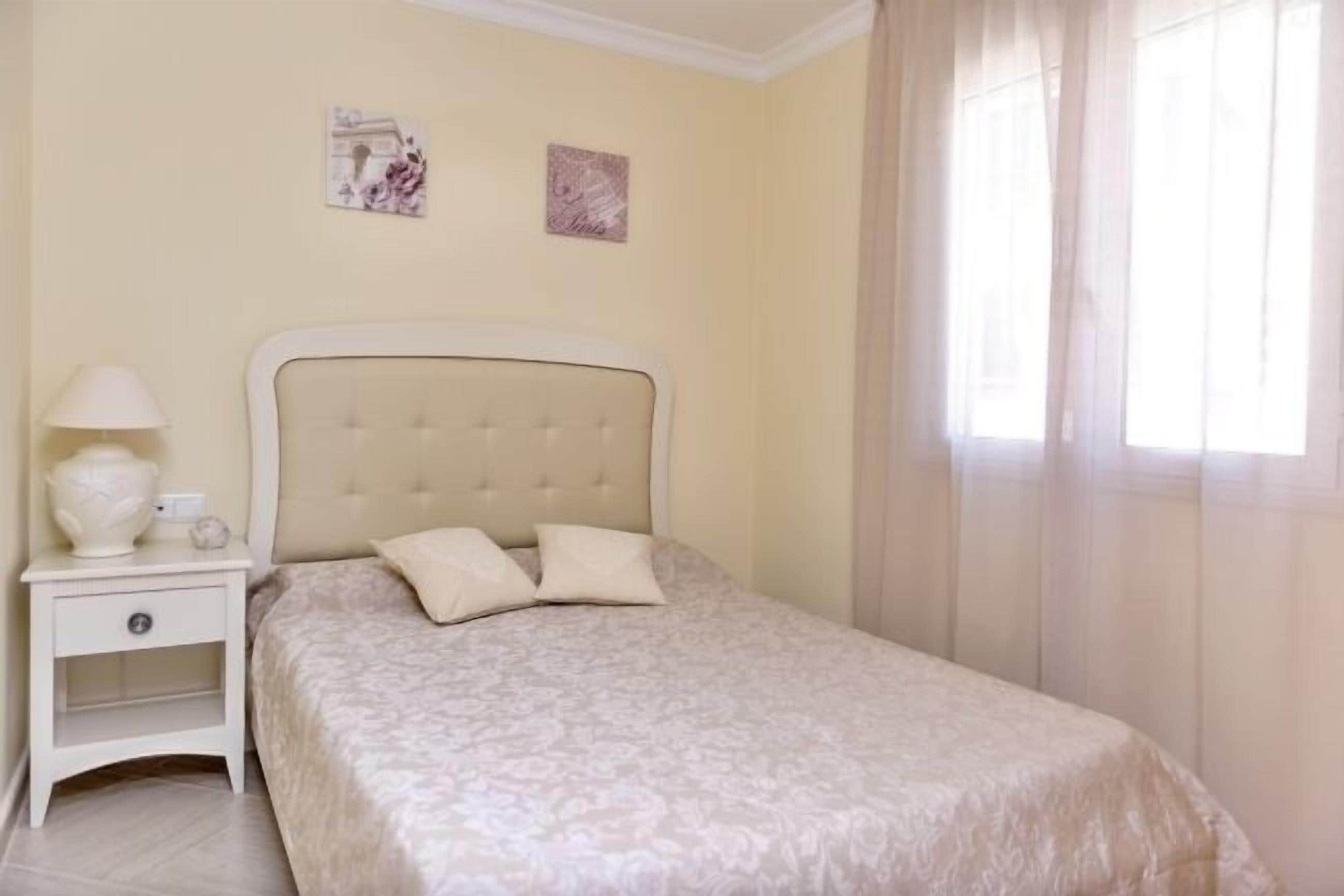 Un dormitorio con cama, mesita de noche y dos obras de arte en la pared.