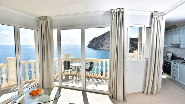 A balcony with a glass table and chairs, a view of the sea, and a kitchen area. - Aparthotel Ola Blanca (Finestrat)