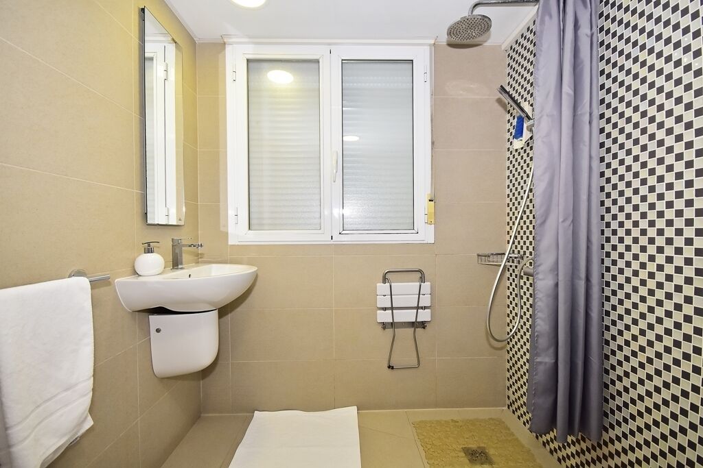 A bathroom with a sink, mirror, window, shower, and tiled walls.
