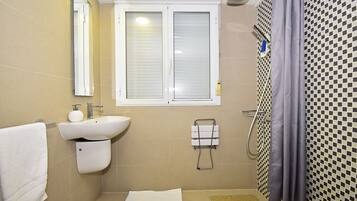 A bathroom with a sink, mirror, window, shower, and tiled walls.