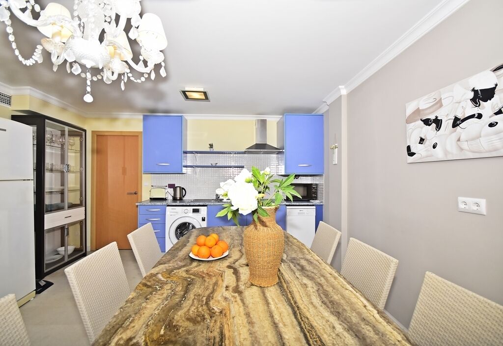 Una cocina moderna con gabinetes azules, una mesa de comedor con un florero y un cuadro en la pared.