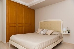 A bedroom with a bed, a nightstand, a lamp, and a wooden wardrobe.