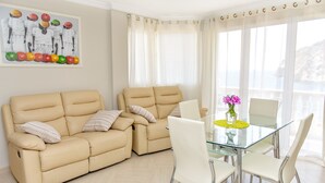 A living room with two beige sofas, a glass dining table with white chairs, and a painting on the wall. - Aparthotel Ola Blanca (Finestrat)