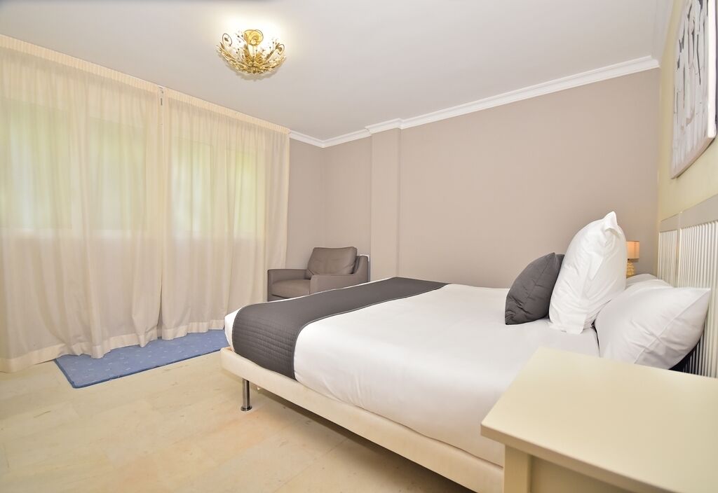 Une chambre d’hôtel avec un lit, une chaise, un bureau et un lustre.