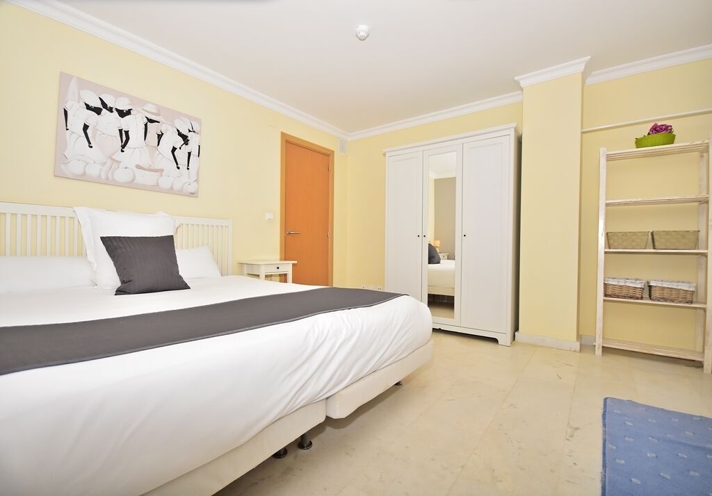 A bedroom with a bed, a wardrobe, a shelf with baskets, and a painting on the wall.