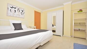 A bedroom with a bed, a wardrobe, a shelf with baskets, and a painting on the wall.