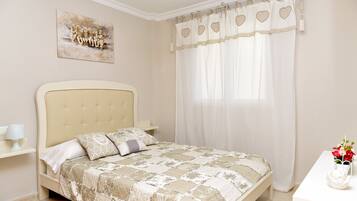 Un dormitorio con cama, mesita de noche, cortinas translúcidas en la ventana y una obra de arte colgada en la pared.