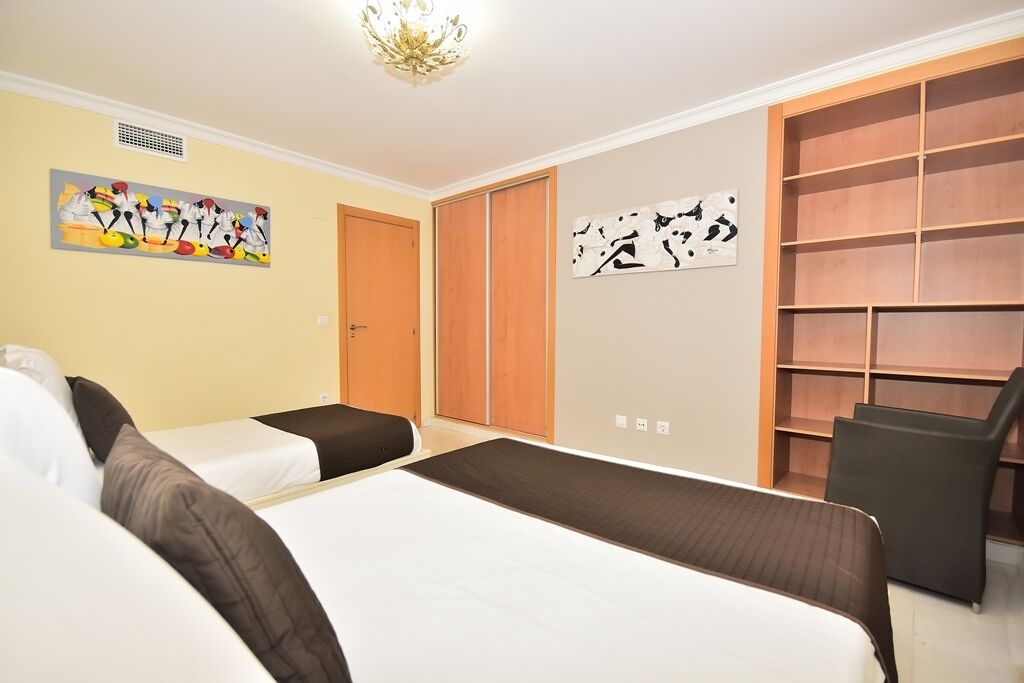 A hotel room with two beds, a wardrobe, a chair, and artwork on the walls.