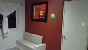 Una habitación con un sofá blanco frente a una pared roja, un cuadro enmarcado encima y una puerta con un letrero verde.