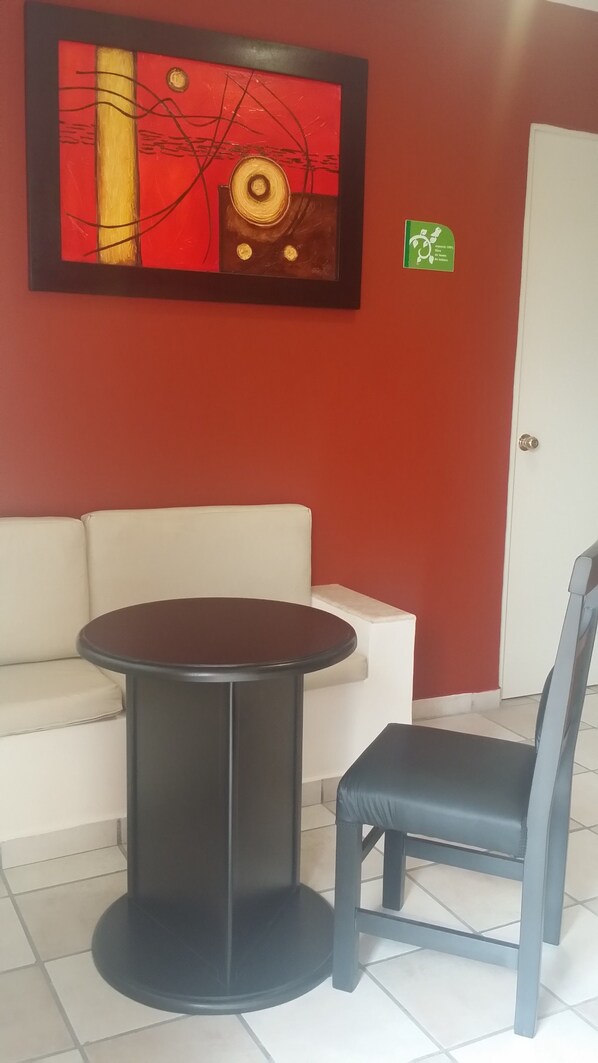 Una habitación con una mesa redonda, una silla, un sofá blanco y una pared roja con un cuadro abstracto enmarcado.