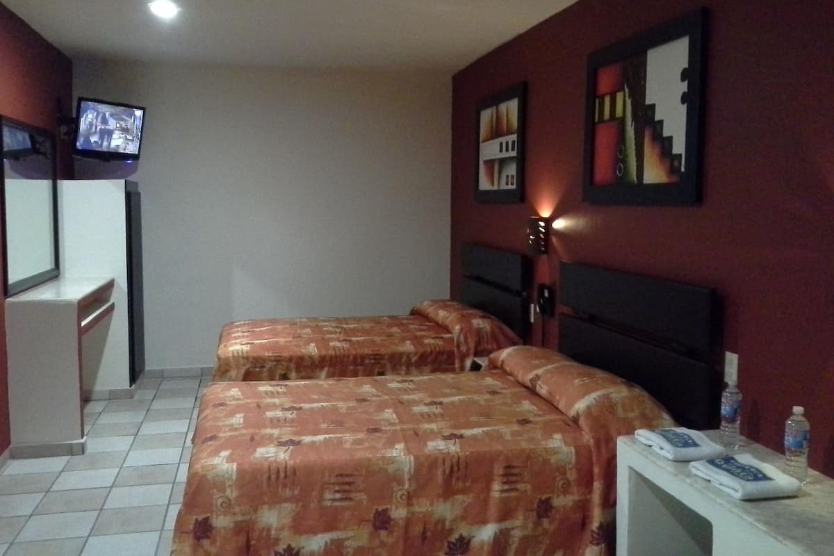 A hotel room with two beds, a desk, a television, and a nightstand with a phone and water bottles.