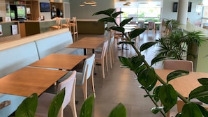 A spacious indoor area with long tables and chairs, a counter with a menu, and large windows allowing natural light.