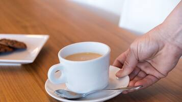 Una taza blanca de café sobre un plato, con una cuchara, sostenida por una mano.